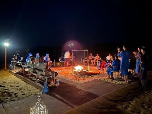 a group of people sitting around a fire on the beach at Morocco wonderland in Merzouga