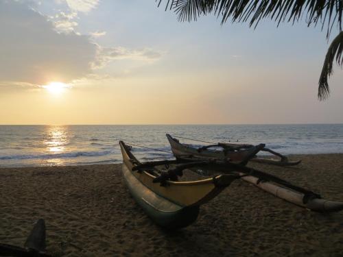 a boat sitting on a beach with the ocean at Karl Holiday Bungalow in Kalutara