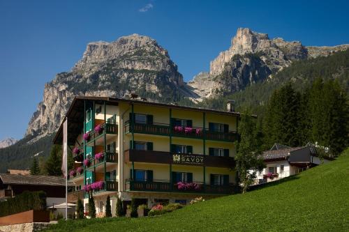 a building on a hill with mountains in the background at Dolomites Wellness Hotel Savoy in La Villa