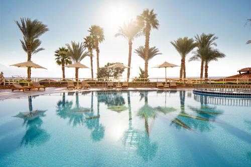 a large swimming pool with palm trees and umbrellas at Steigenberger Hotel & Nelson Village, Taba in Taba