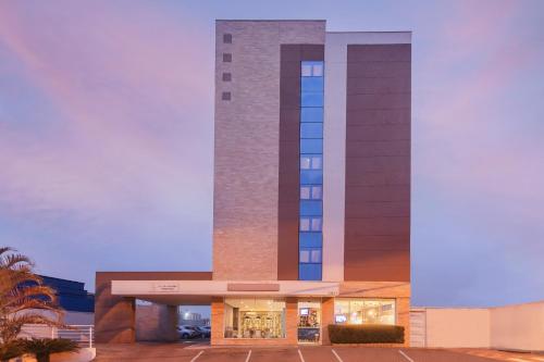 a hotel with a tall tower with a parking lot at Hotel Euro Suite São Jose do Rio Preto by Nacional Inn in Sao Jose do Rio Preto