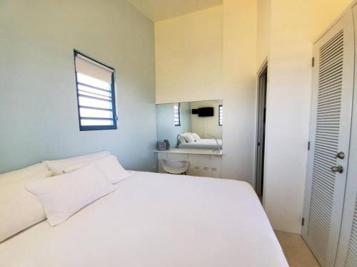 a white bedroom with a white bed and a bathroom at Experience mesmerizing views at The Cliff House from your private plunge pool in Aguadilla
