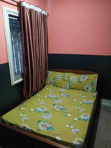 a bed with a yellow comforter and a window at Villa MBOLO in Pointe-Noire