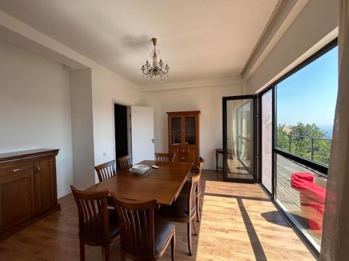 a dining room with a wooden table and a large window at მყუდრო სახლი ფუნიკულიორის პარკთან in Okrokana