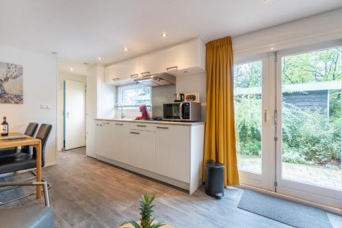 a kitchen with white cabinets and a large window at Bos Chalet Natura - Rust en Natuur op de Veluwe Putten in Putten