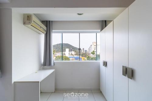 a small white room with a window and a desk at SPT - Studios Convenientes em Blumenau/SC in Blumenau