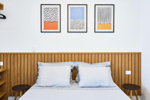 Un dormitorio con una cama con tres cuadros en la pared. en Studio Matira, próximo a praia, novo e moderno, en Ubatuba