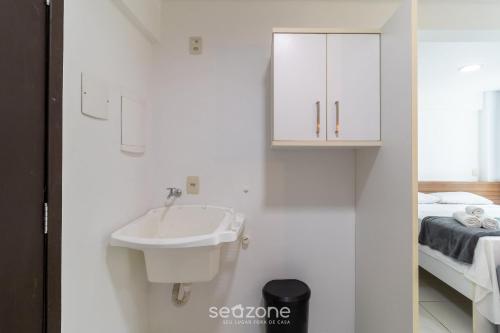 a white bathroom with a sink and a bed at SPT - Studios Convenientes em Blumenau/SC in Blumenau
