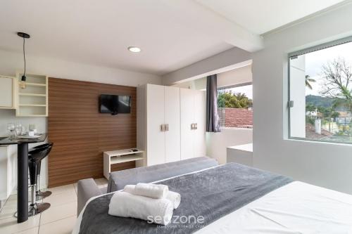 a bedroom with a large bed and a kitchen at SPT - Studios Convenientes em Blumenau/SC in Blumenau