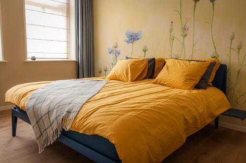 a bedroom with a bed with yellow sheets and flowers on the wall at KorenGastvrij in Noordbroek