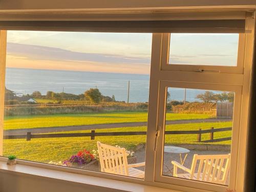 a window with a view of a field and the ocean at Follies Bungalow with Ocean Views in Dungarvan