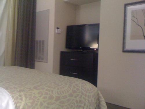 a bedroom with a bed and a flat screen tv at Staybridge Suites Houston Stafford - Sugar Land by IHG in Stafford