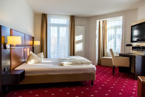 a bedroom with a bed and a desk and a television at Pucci Bärengarten Stadthotel in Ravensburg