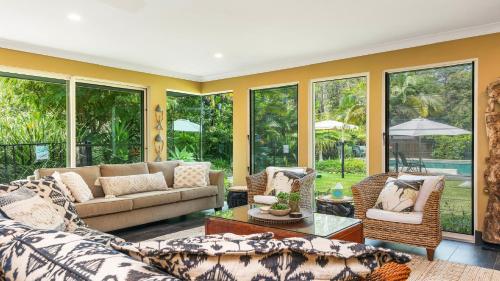 a living room with a couch and chairs and windows at 'Wirreanda Retreat - Acreage' by HolidayCo in Macmasters Beach
