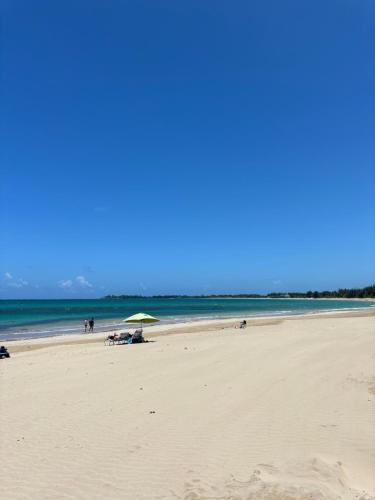 a beach with people sitting on the sand and an umbrella at Isla Verde Modern Apartment with Pool in San Juan