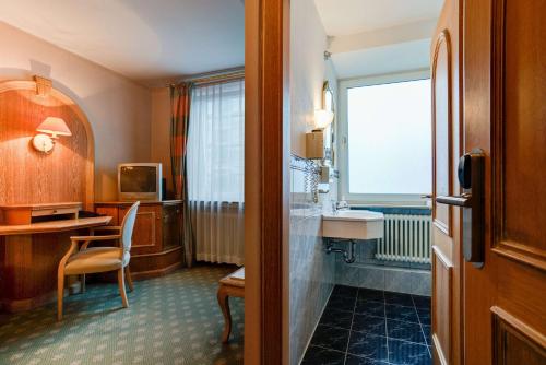 a hotel room with a bathroom with a sink and a desk at Centro Hotel Stern Ulm City, Trademark Collection by Wyndham in Ulm