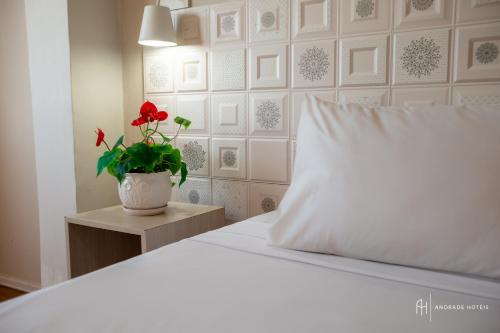 a white bed with a white pillow and a red flower at Rede Andrade Casa Blanca in Fortaleza