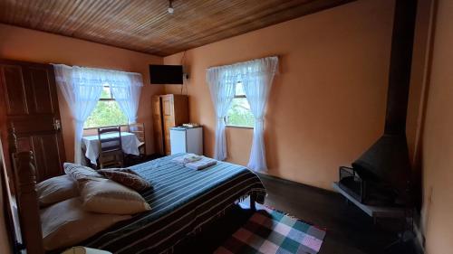 a bedroom with a bed and a desk and windows at Pousada Pedra da Gávea in Visconde De Maua
