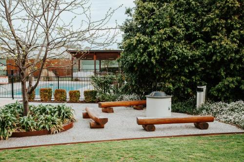 two wooden benches in a park with a trash can at Nagambie Waterfront Motel in Nagambie