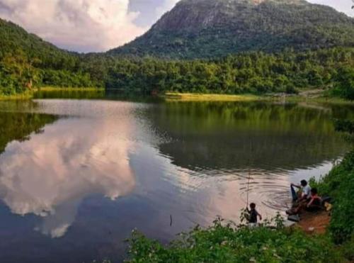 a group of people sitting on the shore of a lake at PALASH Pahar Resort in Jhalida