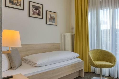 a bedroom with a bed and a chair and a window at Sautter Hotel Stuttgart City in Stuttgart