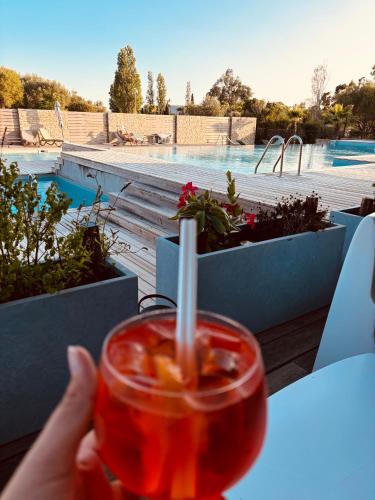 une main tenant un verre avec vue sur la piscine dans l'établissement La Villa Sylody restaurant, 3 piscines et location de vélo sur place, à Lecci