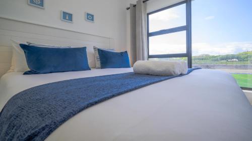 a bedroom with a bed with blue pillows and a window at Ballito Village Luxury Apartments in Ballito