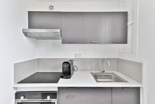 une cuisine blanche avec un évier et un plan de travail dans l'établissement Studio tout équipé à Montreuil proche Paris - II, à Montreuil