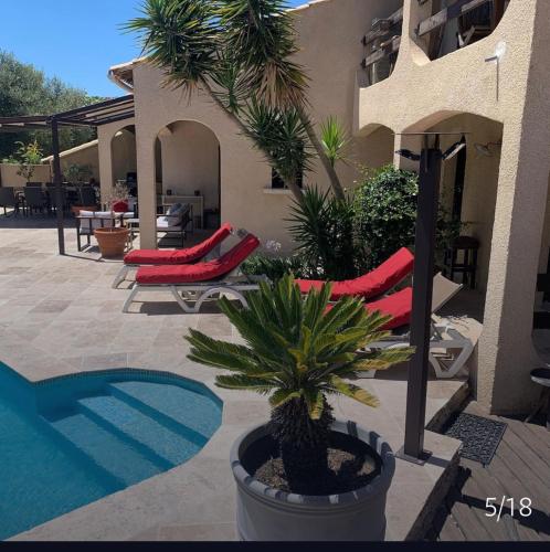 un patio avec deux chaises rouges et un palmier dans l'établissement Villa Jean Mira, à La Grande Motte