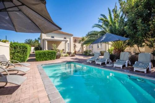 a swimming pool with chairs and an umbrella at Somerset Wineland Apartments & Wellness in Somerset West