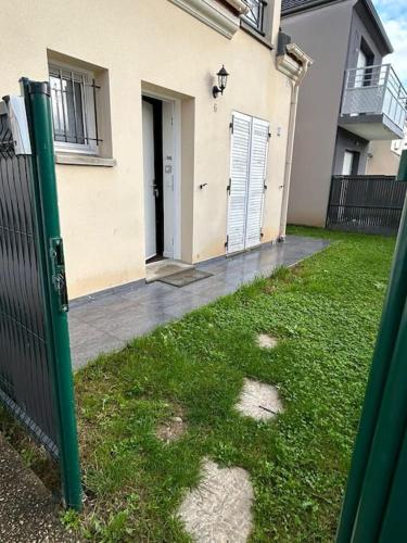 a house with a gate in the grass next to a building at Résidence paisible 3 chambres 30 Min Aéroport Roissy CDG in Persan
