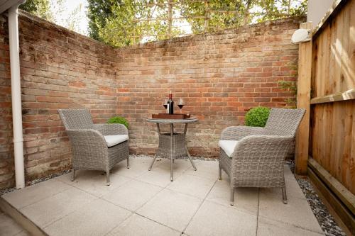 a patio with three chairs and a table with a brick wall at Central Medieval Grid Unique home with Gated parking in Bury Saint Edmunds