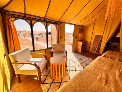 a room with a bed and chairs in a tent at Merzouga Glamping With AC in Merzouga