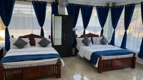 two beds in a bedroom with blue curtains at Chan Beach Resort & Hotel in Bahūr