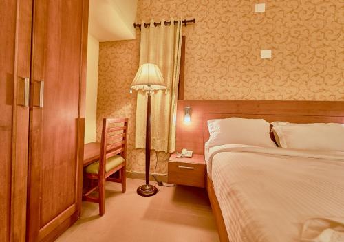 a bedroom with a bed and a desk and a lamp at Ushasree Wayanad Pool Resort by VOYE HOMES in Ambalavayal