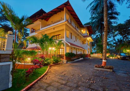a large building with palm trees in front of it at Ushasree Wayanad Pool Resort by VOYE HOMES in Ambalavayal