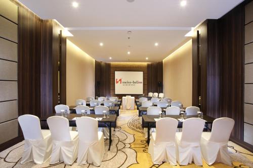 a conference room with tables and white chairs and a screen at Swiss-Belinn Karawang in Karawang