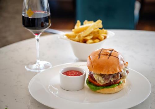 a plate with a hamburger and french fries and a glass of wine at The College Green Dublin Hotel, Autograph Collection in Dublin