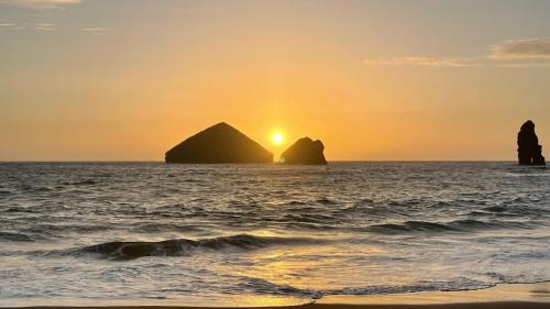 a sunset over the ocean with two large rocks at La VIGIE de CASTELROCK ( Casa Petunia ) in Mosteiros