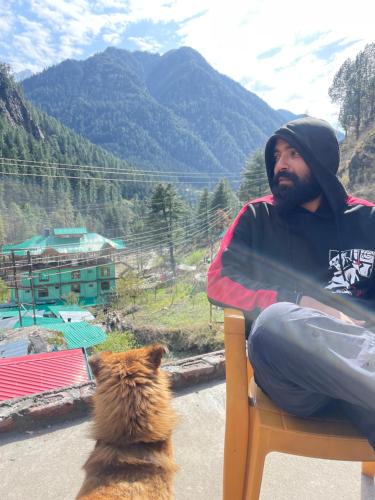 a man sitting in a chair next to a cat at Trippy Homestay in Kasol