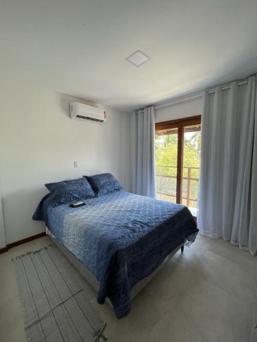 a bedroom with a bed with a blue comforter and a window at Residencial VillaBella casa 3 Quartos, piscina, na Vila junto ao Centro e Praia in Marau