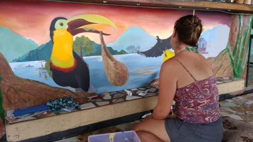 a woman sitting in front of a painting of birds at Hostal Portobelo in Portobelo