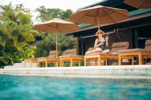 a woman sitting on a chair next to a swimming pool at Hotel Three Sixty - Adults Only in Ojochal