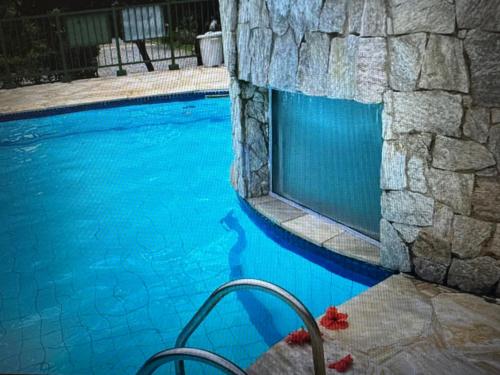 a swimming pool with blue water and a stone wall at Casa 3 Quartos com Espaço Gourmet - Bairro Ferradura in Rio de Janeiro