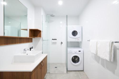 a white bathroom with a washing machine and a sink at Abode Malua Bay in Malua Bay