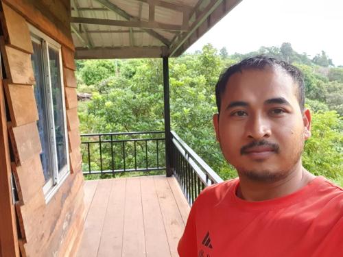 a man in a red shirt standing on a balcony at Banlung Mountain View Treks & Tours in Banlung