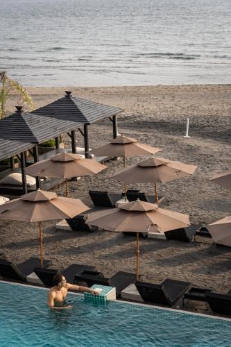 a man in a swimming pool next to a beach with umbrellas at Bayandati Resort in Bataan