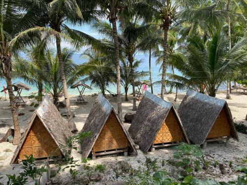 a group of huts on a beach with palm trees at Alfonsa Tent Ground - Camp By The Sea in Oslob