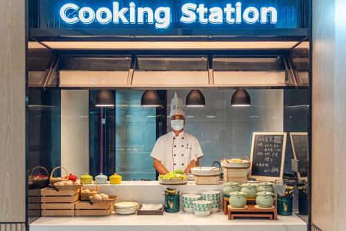 a chef wearing a mask standing in a cooking station at Echarm Hotel Guangzhou Baiyun Station Julong Metro Station in Guangzhou
