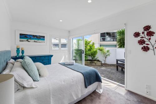 a white bedroom with a bed and a patio at The Dunes - Whangamata Holiday Apartment in Whangamata